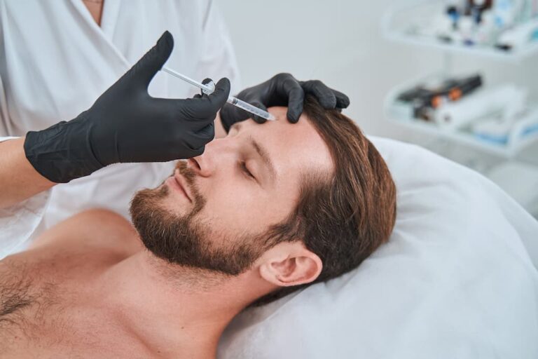 A man lying on a treatment bed receives a dermal filler injection in his forehead from a professional wearing black gloves, aiming to smooth forehead lines.