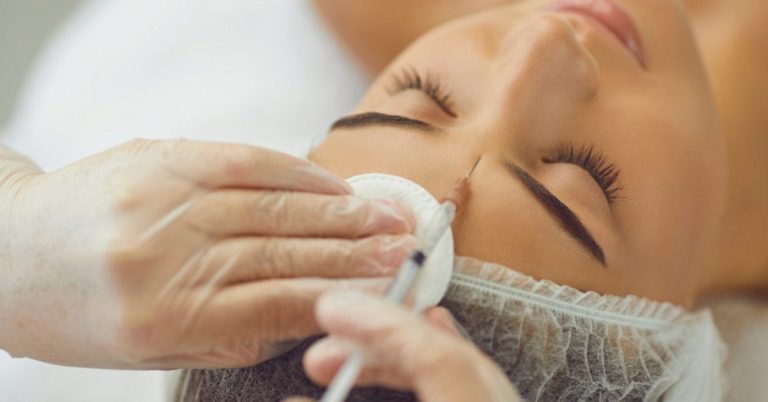 Woman lying down with eyes closed while a provider applies treatment to her face