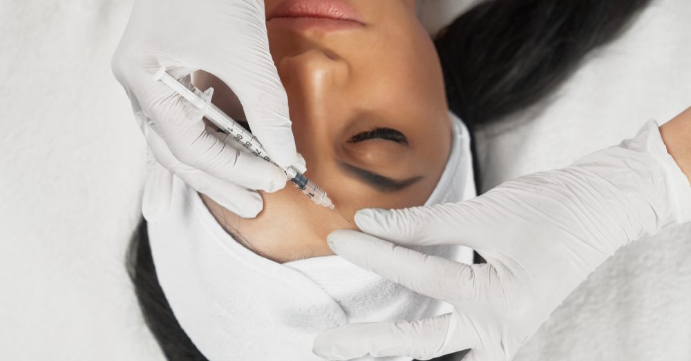 Woman receiving a cosmetic injection near the forehead area from a gloved provider in a clinical setting