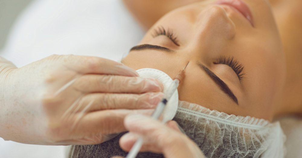 Woman lying down with eyes closed while a provider applies treatment to her face