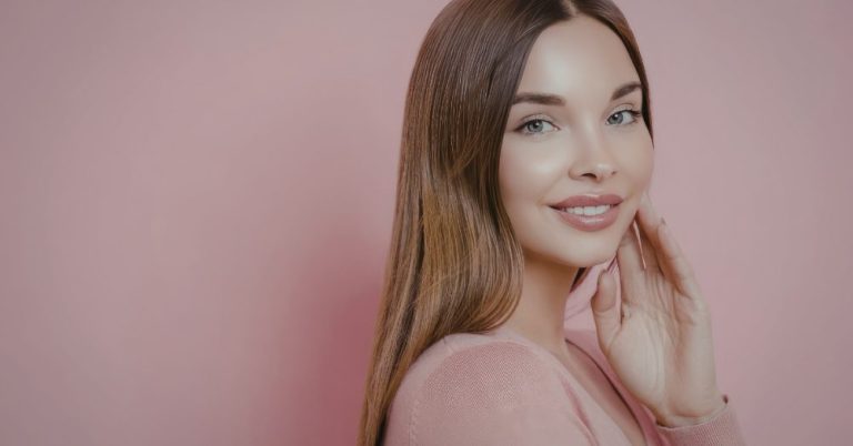 Woman with clear, smooth skin touching her face against a pink background
