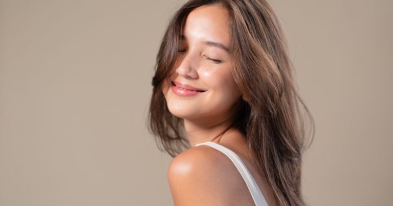 Woman against a neutral background smiling with her eyes closed
