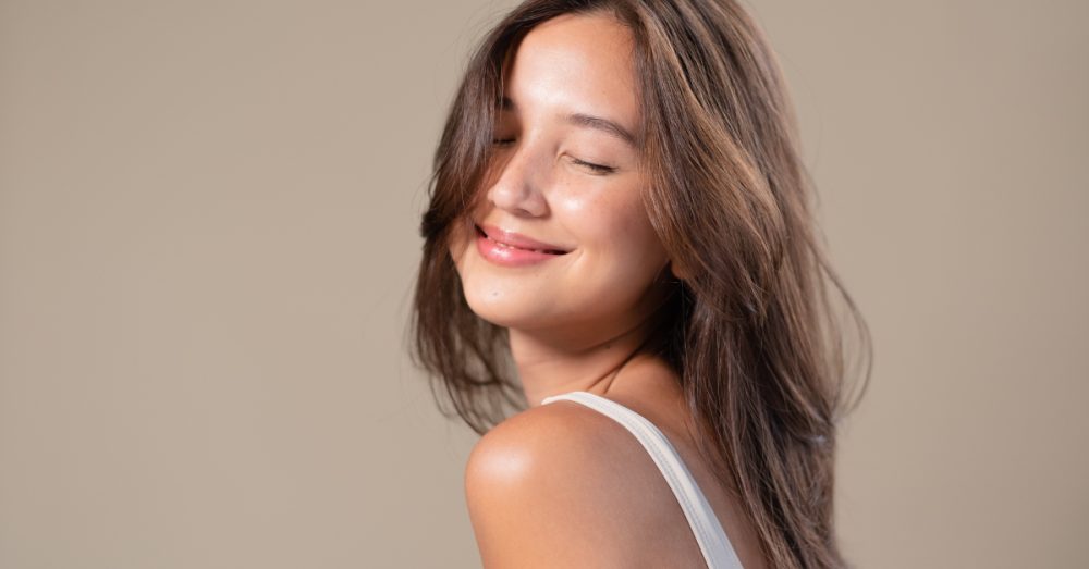 Woman against a neutral background smiling with her eyes closed